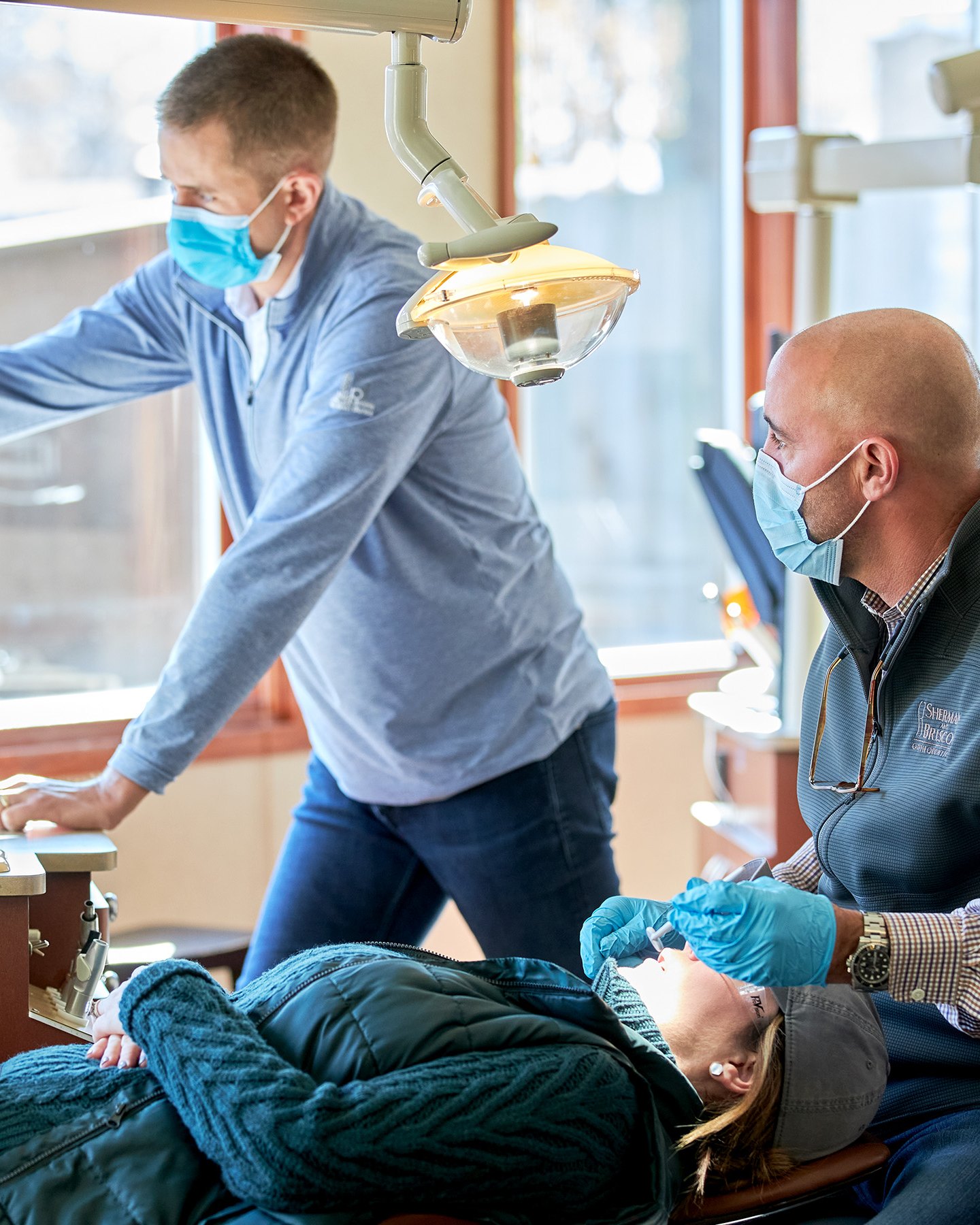 Two Sherman & Briscoe orthodontists caring for a patient in a sunlit treatment room.
