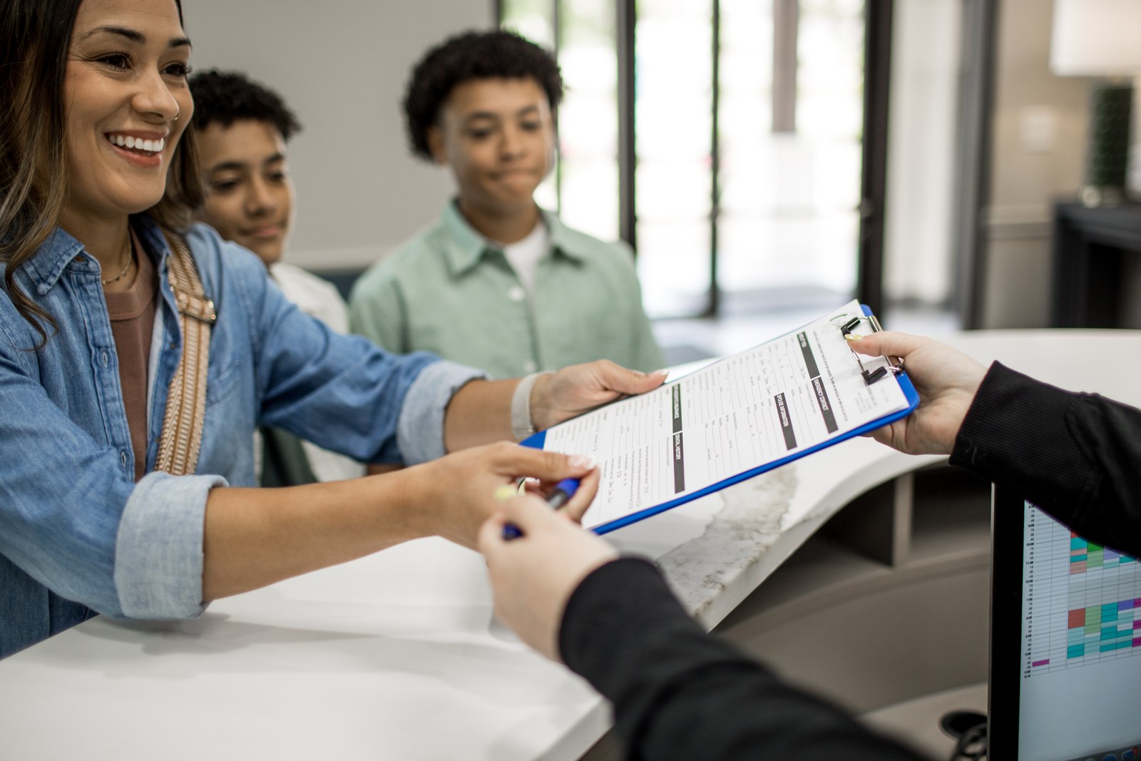 A parent and two teenage patients checking in at the front desk.